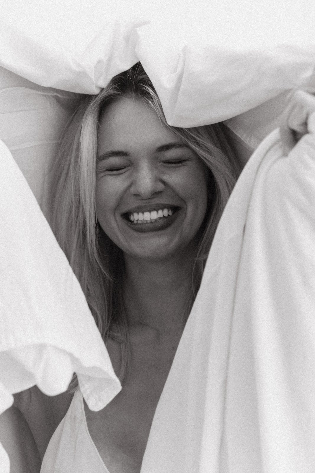 Woman laughing under a white duvet