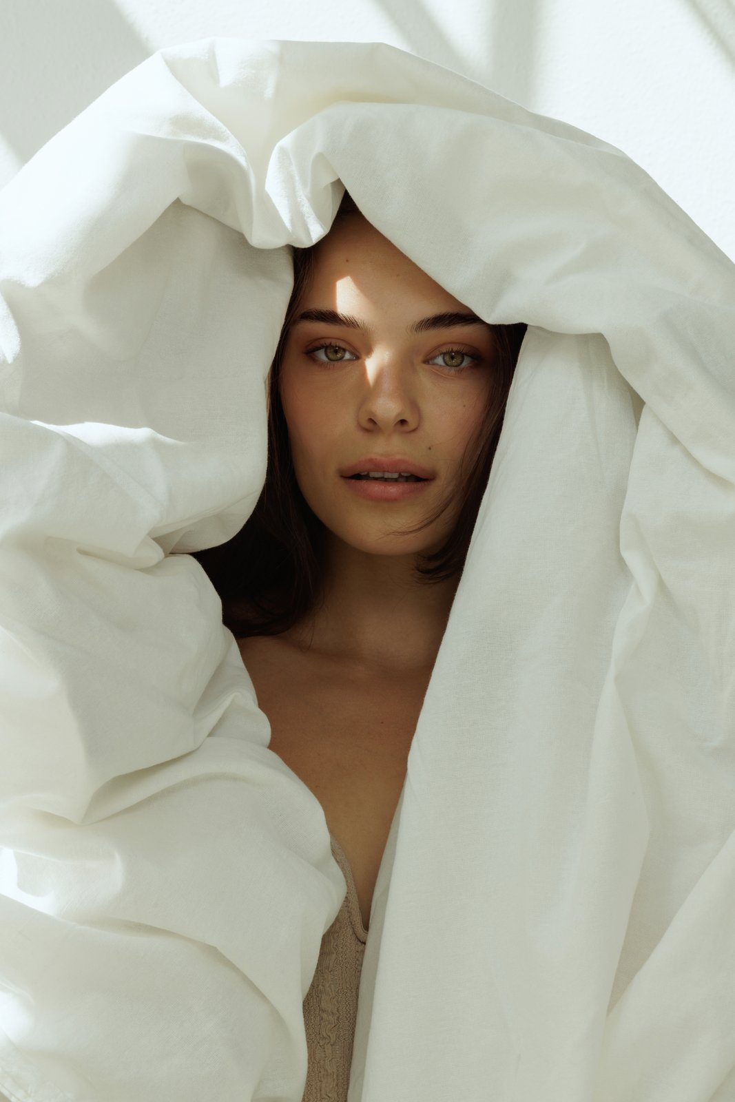 Brunette woman peeking out from under a duvet